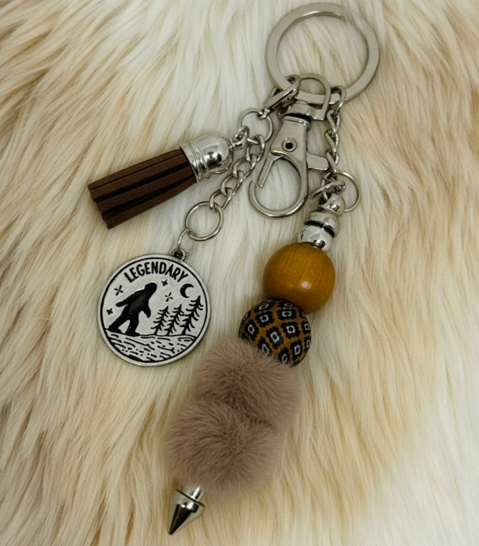 Big Foot Keychain with tassel, wooden bead, and decorative charm on a fur background