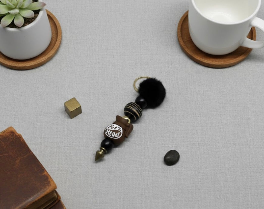 Pot Head Keychain with decorative elements on a gray surface with a cup and plant in the background