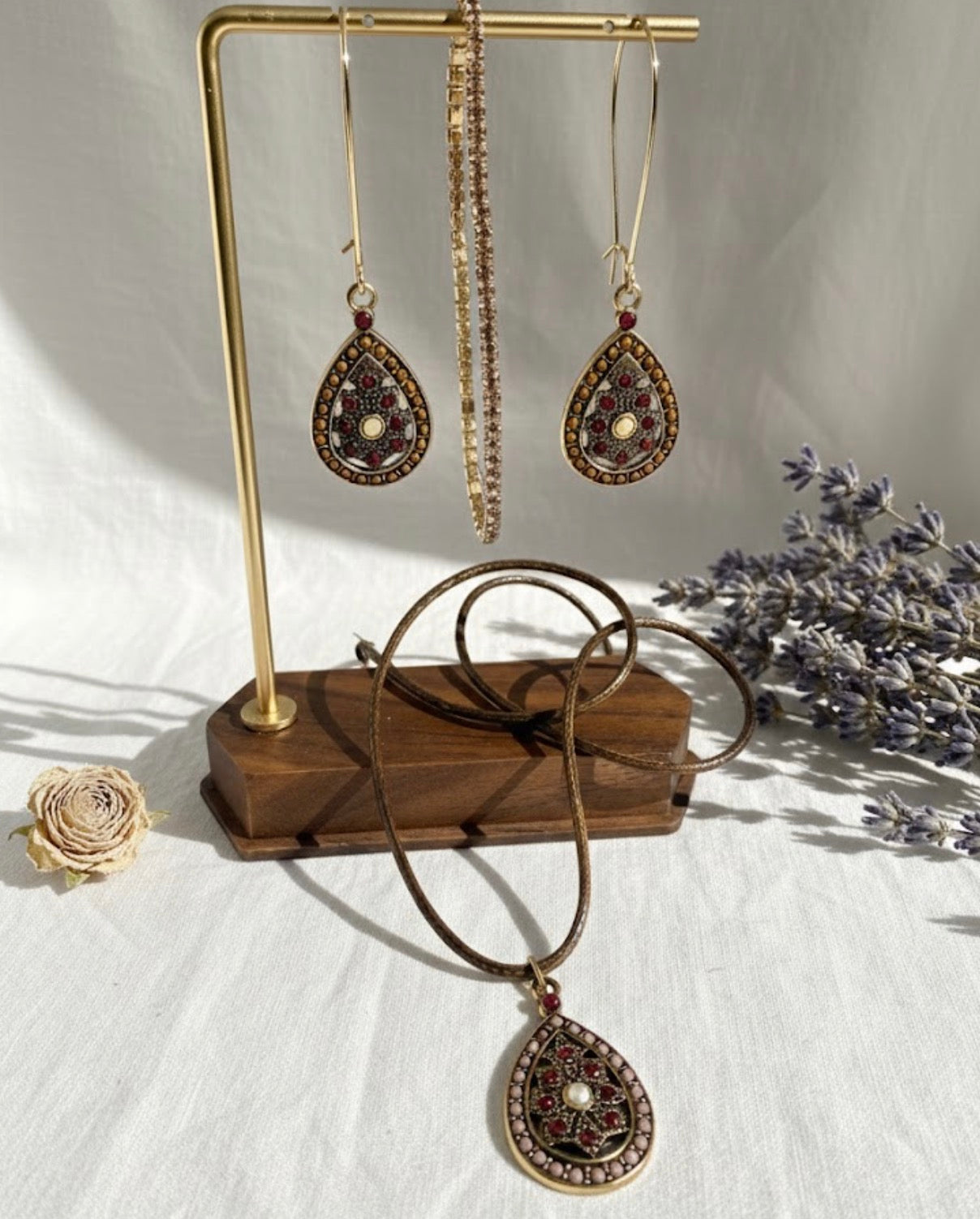 Jewelry set with mandala earrings and necklace on a stand with lavender flowers in the background.
