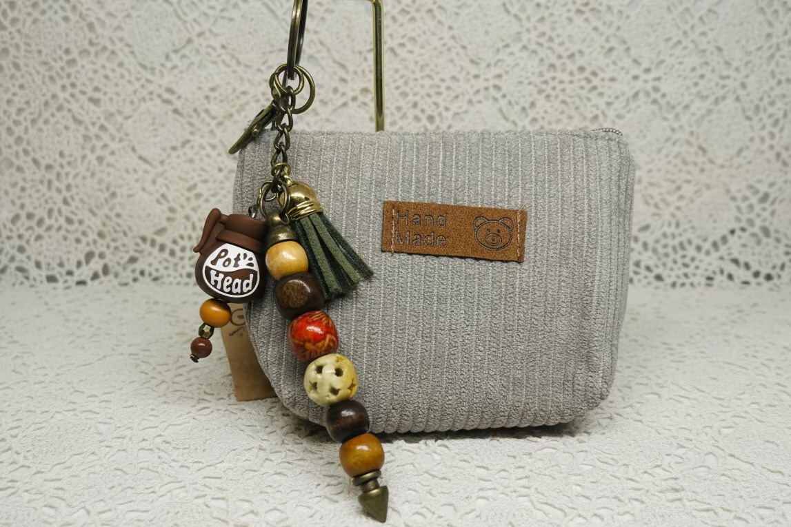 Pot Head Coffee Pot Keychain with beads and tassel attached to a gray textured pouch on a white background