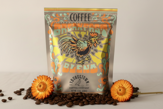 Coffee bag with rooster design on a beige background with coffee beans and flowers.