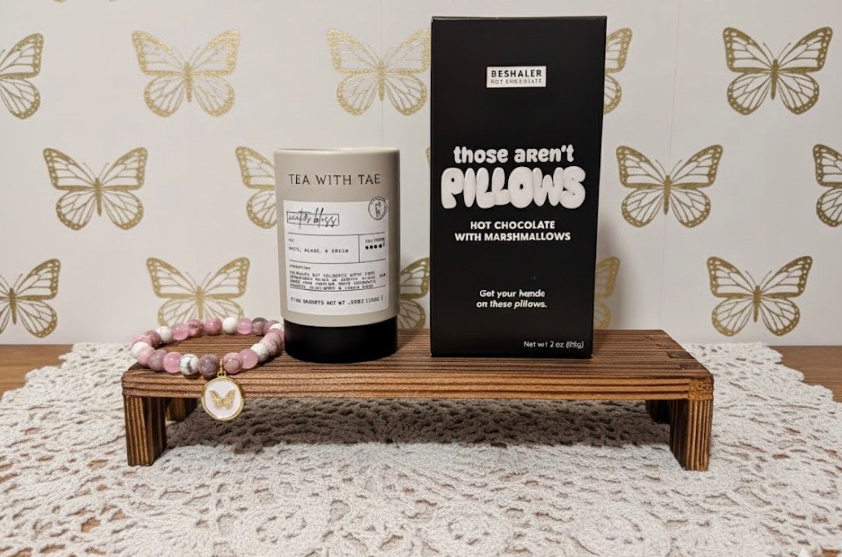 Tea container and box of Those Aren’t Pillows hot chocolate on a wooden stand with butterfly-patterned wallpaper.
