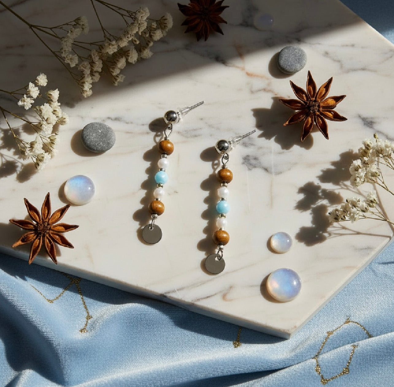 Pair of beaded earrings on a marble surface with dried flowers and spices.