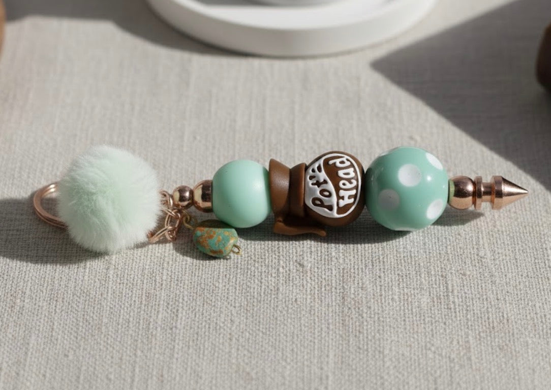 Coffee Pot Head Keychain with pom-pom and beads on a light surface