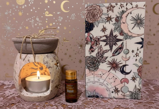 Aromatherapy diffuser with a lit candle next to a box with celestial designs on a patterned surface.