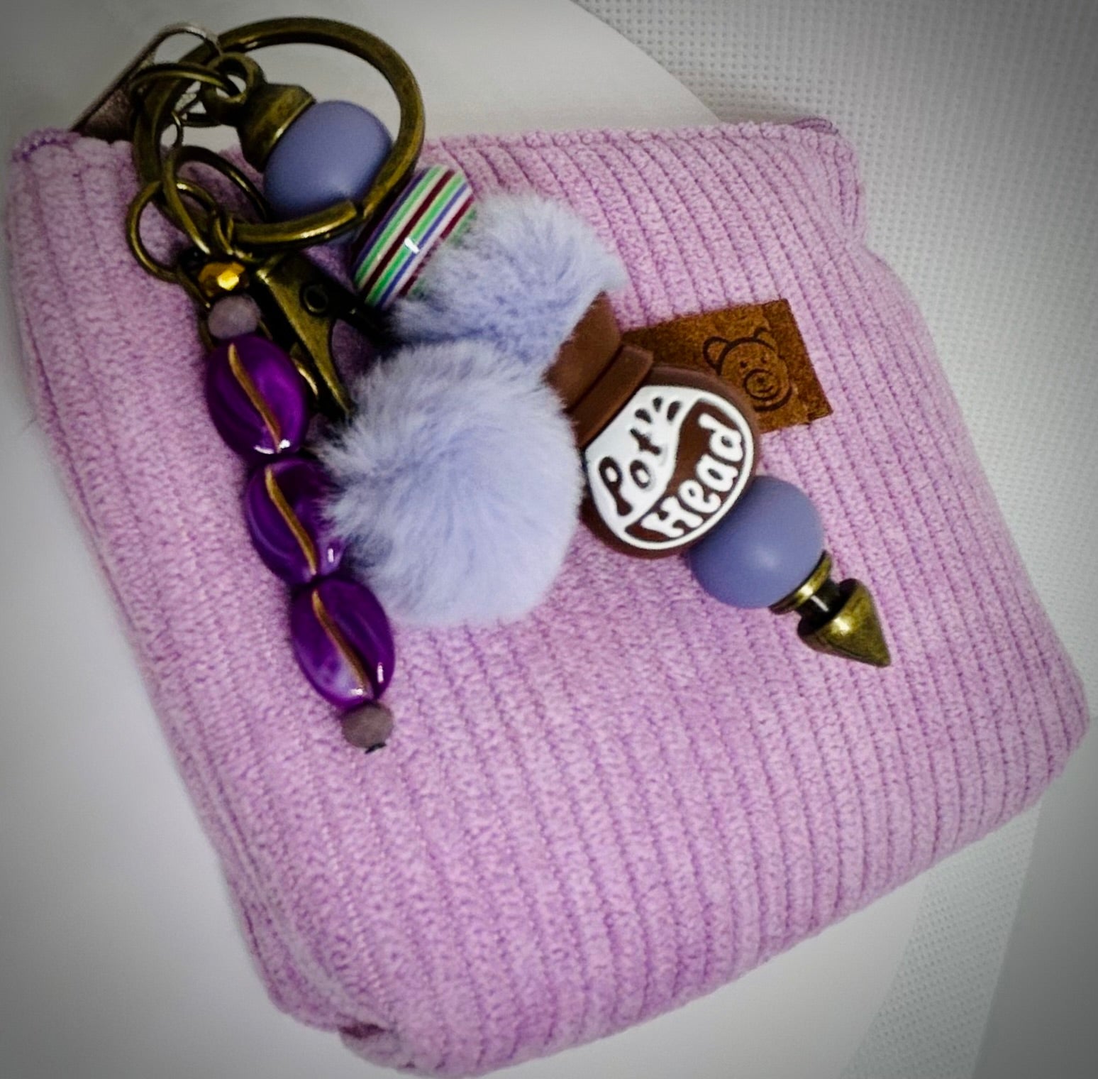 Pot head coffee pot Keychain with purple beads and fluffy charm on a pink textured surface. Pot head. 