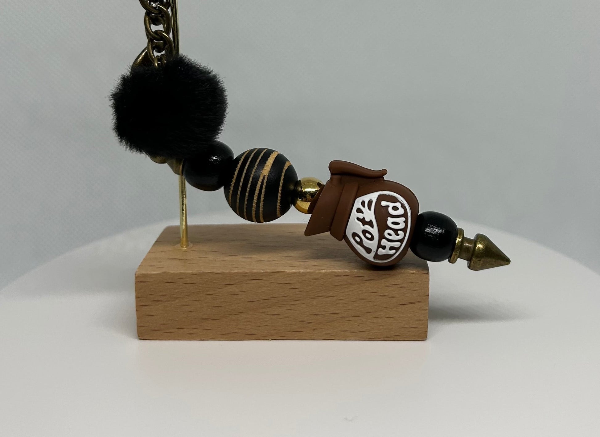 Decorative pot head bag charm keychain with black beads and a wooden base on a gray background