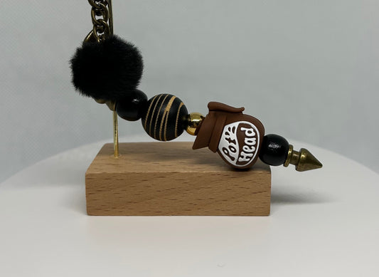 Decorative pot head bag charm keychain with black beads and a wooden base on a gray background