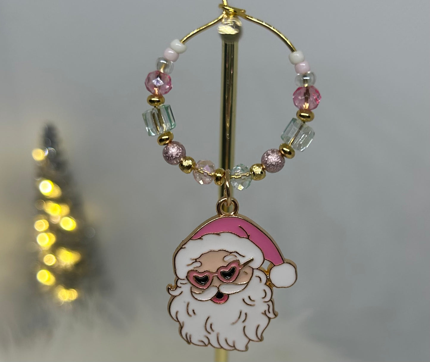 Wine glass charm with pink Santa Claus charm and heart shaped sunglasses on a beaded hoop on a blurred background. Pink. Mint green. 