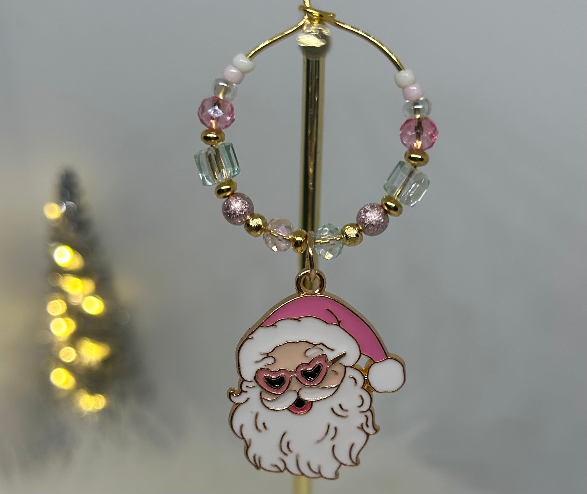 Wine glass charm with pink Santa Claus charm and heart shaped sunglasses on a beaded hoop on a blurred background. Pink. Mint green. 