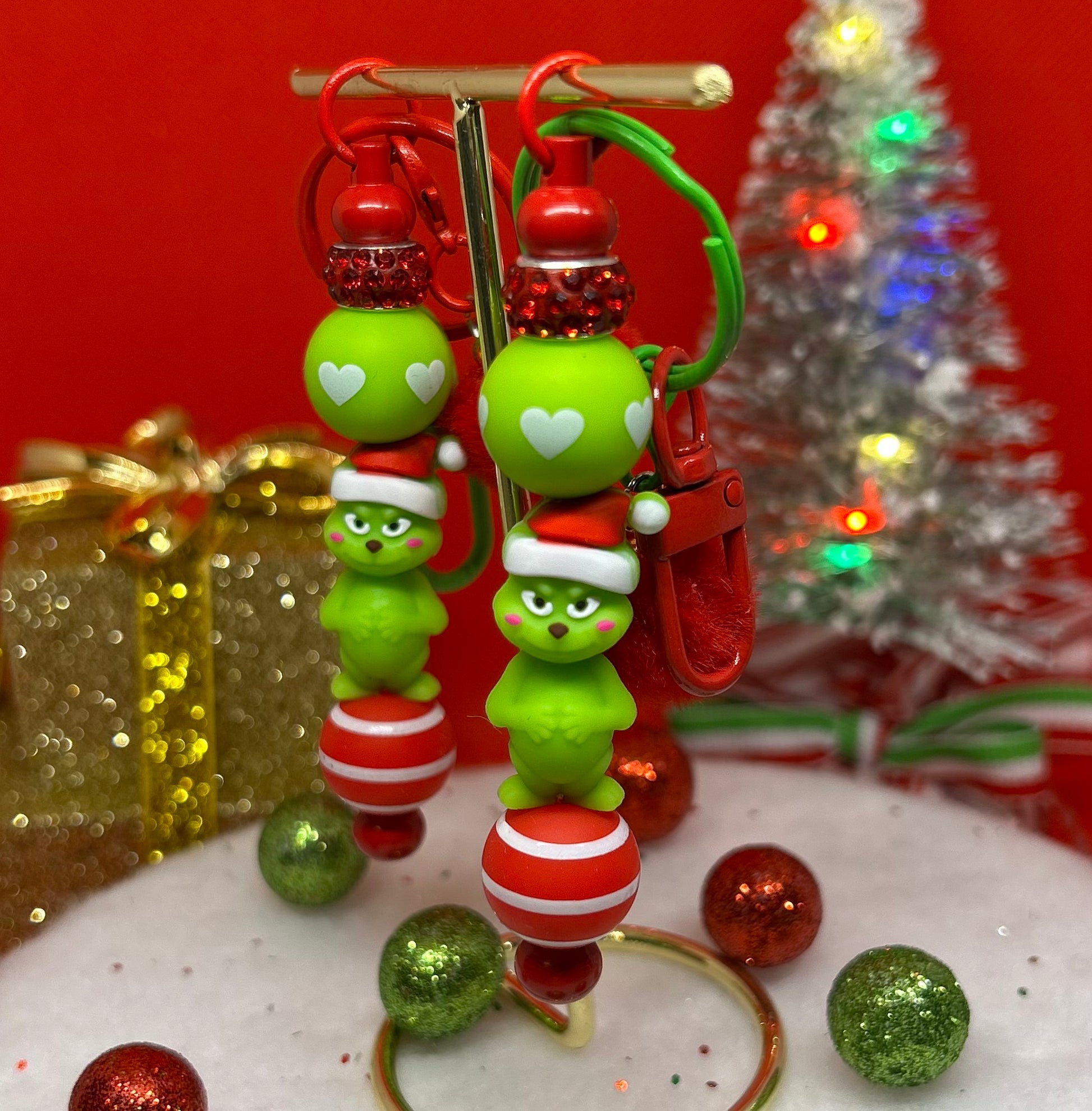 Grinch keychain bag charm with green characters and red accents on a reflective surface with Christmas decorations in the background.