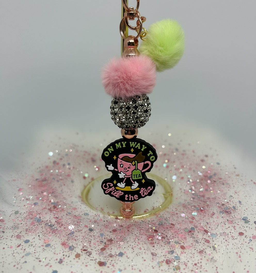 Keychain with colorful pom-poms and character design on a white background. Spill the tea. Faux fur. Rhinestone bead. 