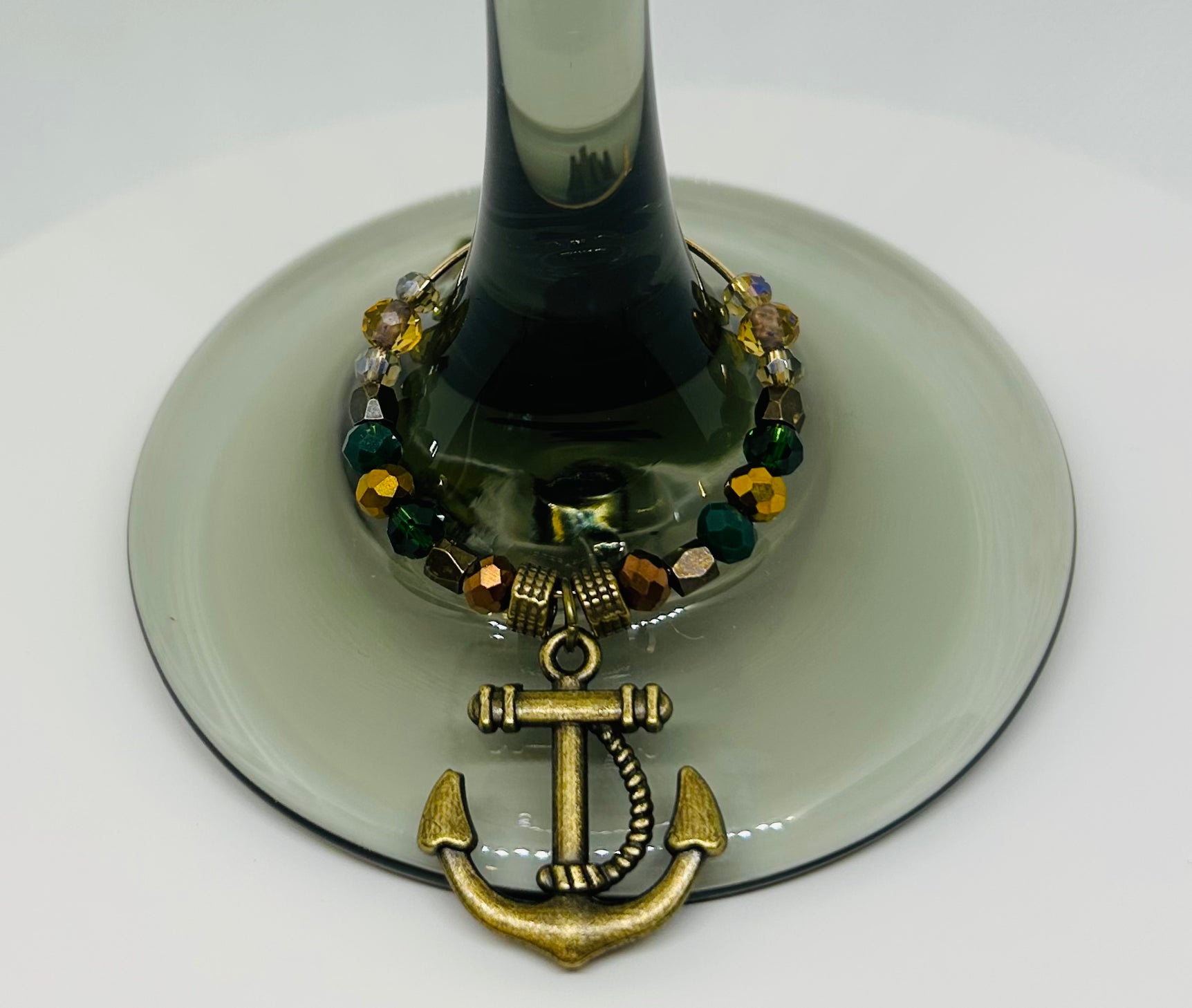 Decorative wine glass charm with an anchor design on a white background on a wine glass. Ancient bronze. Glass beads. 