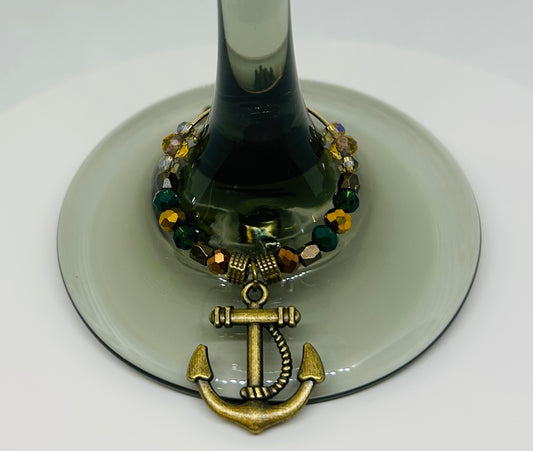 Decorative wine glass charm with an anchor design on a white background on a wine glass. Ancient bronze. Glass beads. 