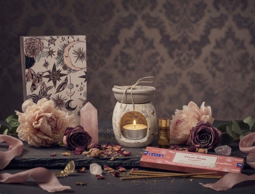 Aromatherapy soapstone setup with a tealight candle, oils, flowers, and incense on a dark surface.