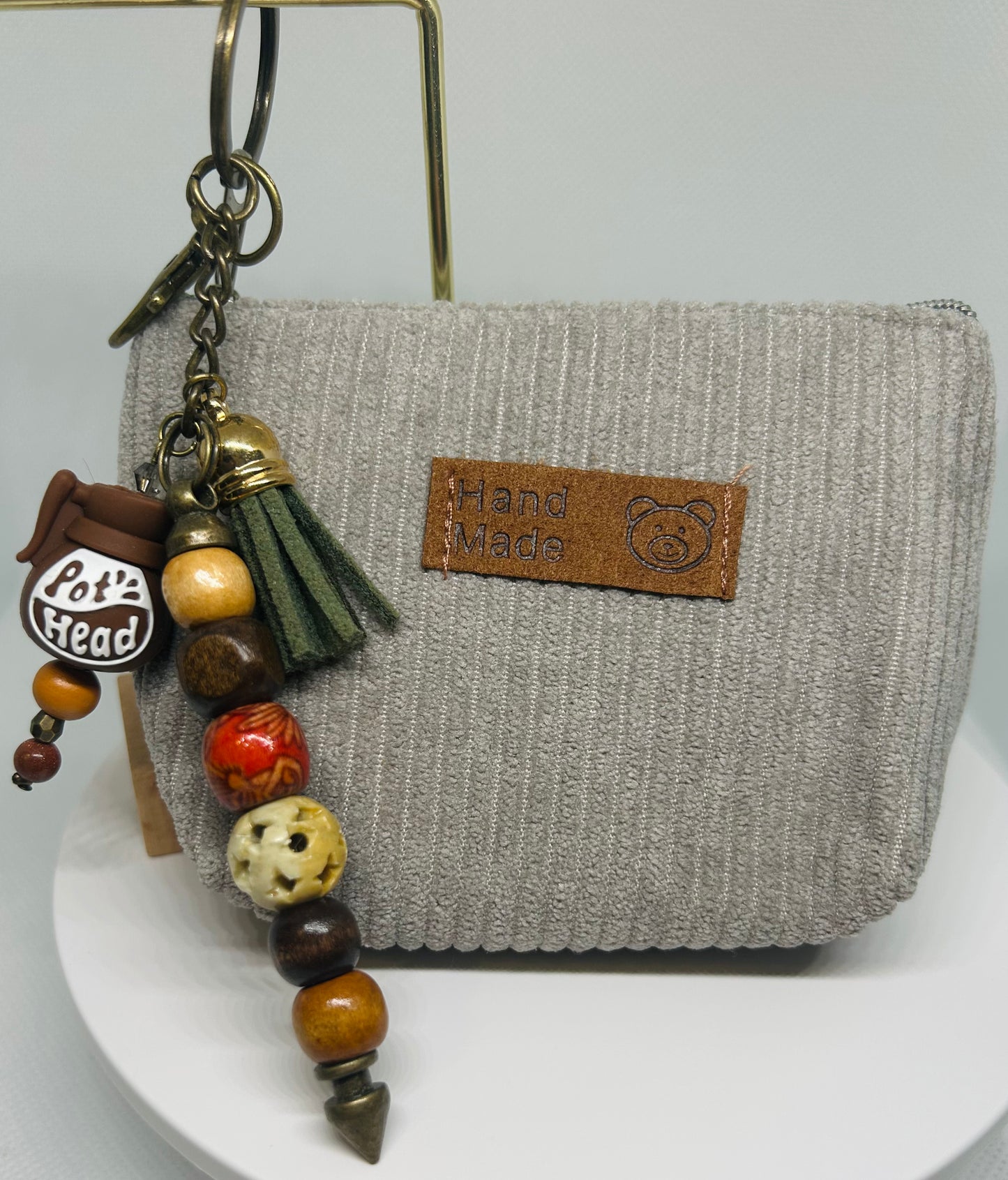 Pot Head Coffee Pot Keychain with beads and tassel attached to a gray textured pouch on a white background