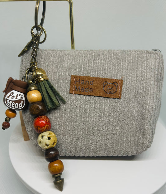 Pot Head Coffee Pot Keychain with beads and tassel attached to a gray textured pouch on a white background