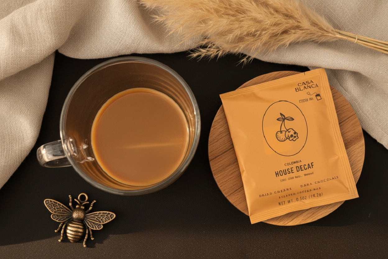 Clear mug with dried cherry and dark chocolate steeped coffee next to a package of House Decaf coffee on a dark surface.