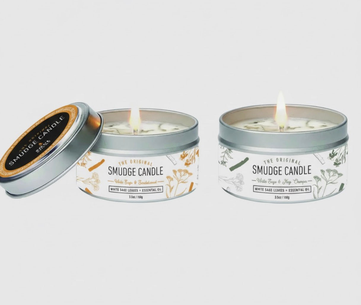 Two smudge candles in metal tins with decorative labels on a white background