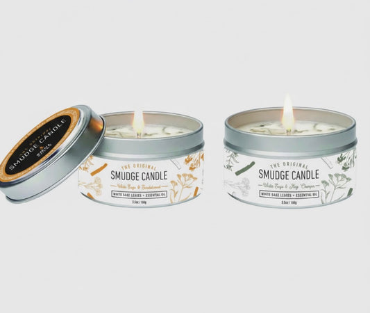 Two smudge candles in metal tins with decorative labels on a white background