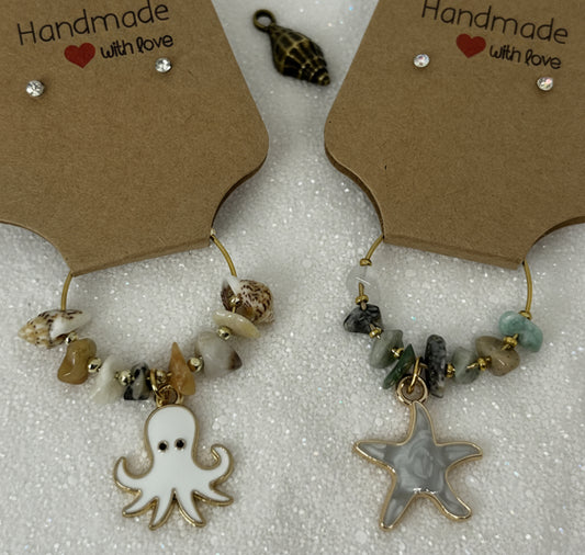 Pair of handmade wine glass charms with starfish and octopus charms on a textured surface.