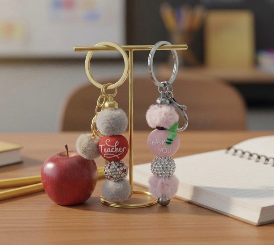 Two Teacher Appreciation keychains on a stand with an apple and books in the background