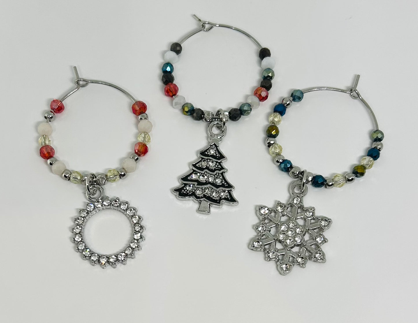 Set of three wine glass charms with Christmas-themed pendants on a white background. tree. snowflake. wreath. 