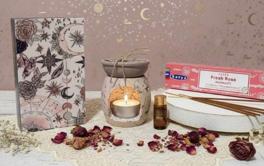 Aromatherapy setup with soapstone burner, candle, essential oil, ash catcher, and incense on a decorative surface.