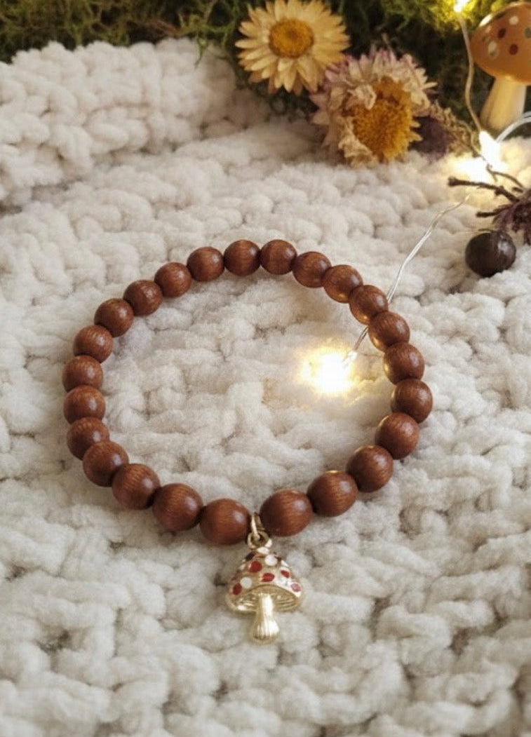 Wooden beaded bracelet with a decorative mushroom charm on a textured surface with flowers in the background