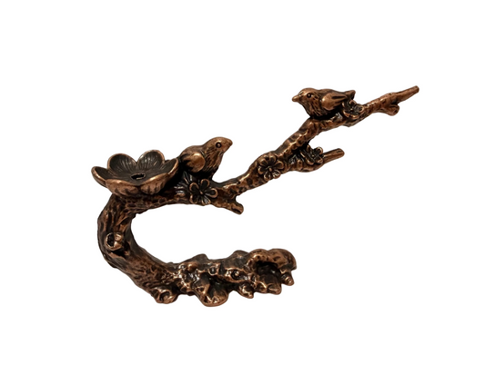 Bronze incense cone holder of birds on a branch with flowers against a neutral background