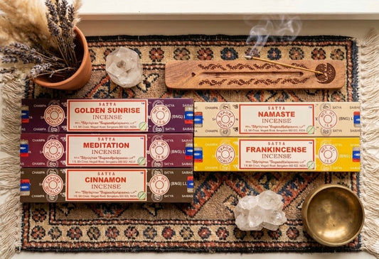 Incense sticks with packaging on a decorative mat with a wooden spoon and flowers.