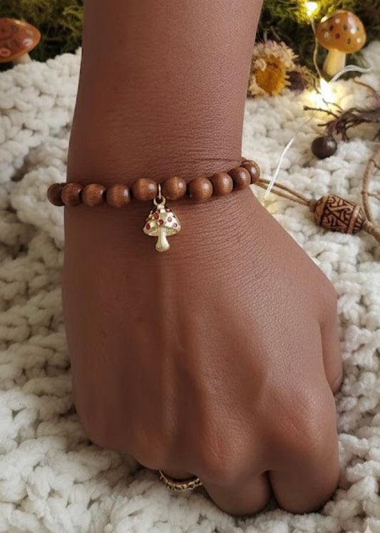 Brown wooden beaded bracelet with a charm on arm against a textured white surface.