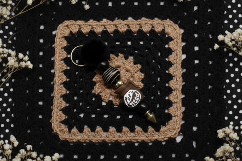Pot Head Keychain on Crocheted square with decorative items on a black and white polka dot background