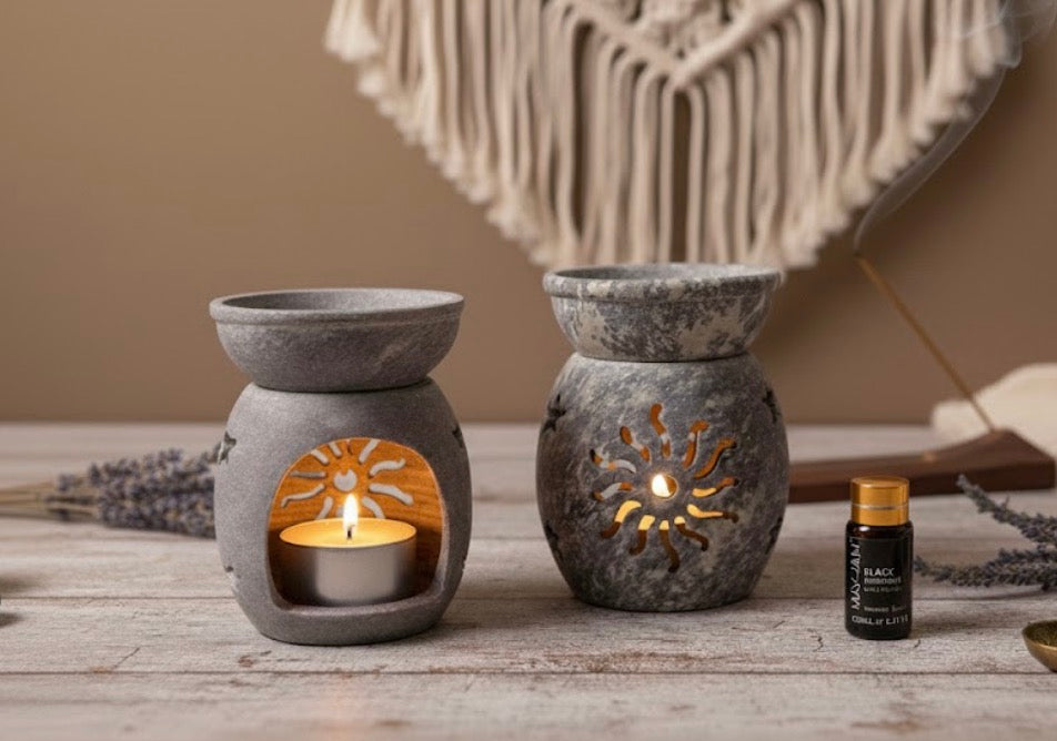 Two soapstone oil burners with candles and a bottle of essential oil on a wooden surface.