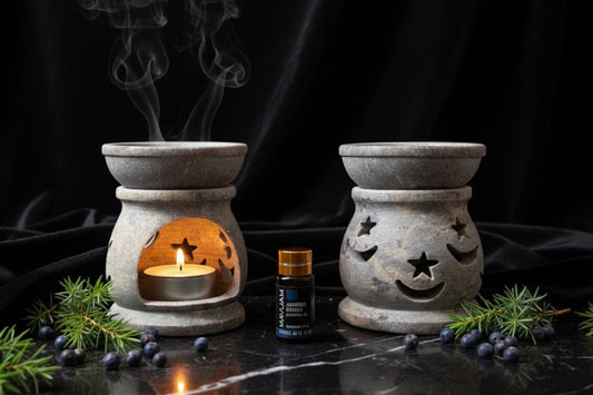 Two soapstone essential oil burners with one lit candle and essential oil bottle on a dark surface.