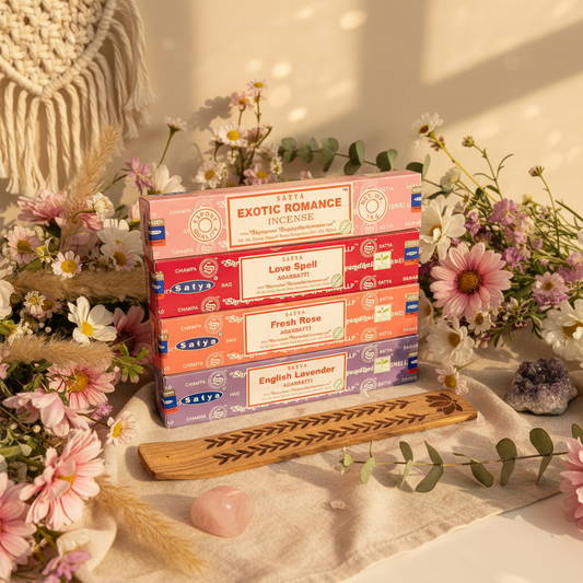 Stack of Satya incense boxes with a wooden incense holder on a decorative surface with flowers.