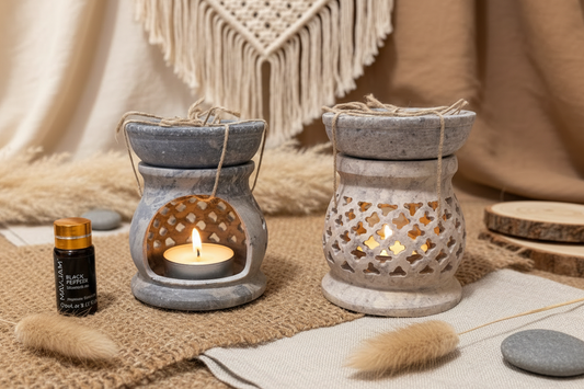 Two soapstone oil burners with candles on a textured surface, surrounded by decorative items.