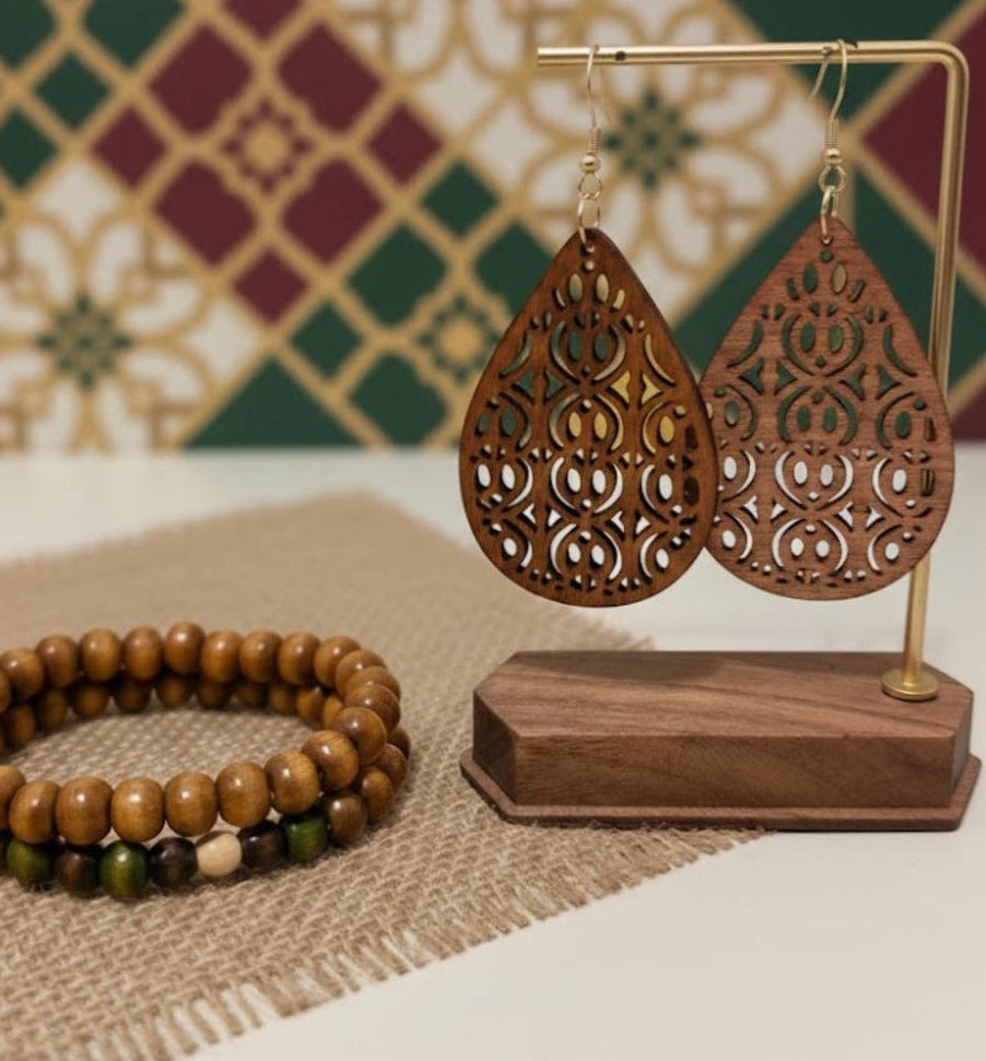 Wooden earrings on a stand with a bracelet on a textured surface and patterned wall in the background
