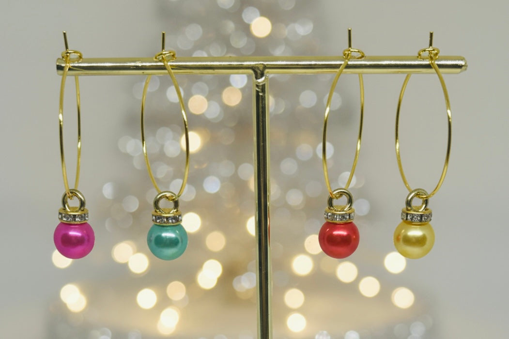 Gold wine glass charms with colorful Christmas ornament beads on a gold stand against a blurred light background