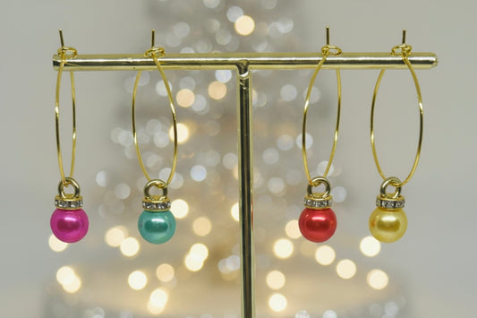 Gold wine glass charms with colorful Christmas ornament beads on a gold stand against a blurred light background