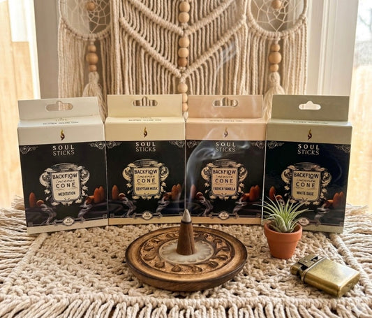 Four boxes of 'Soul Sticks' incense cones on a textured surface with a wooden incense burner and small plant.