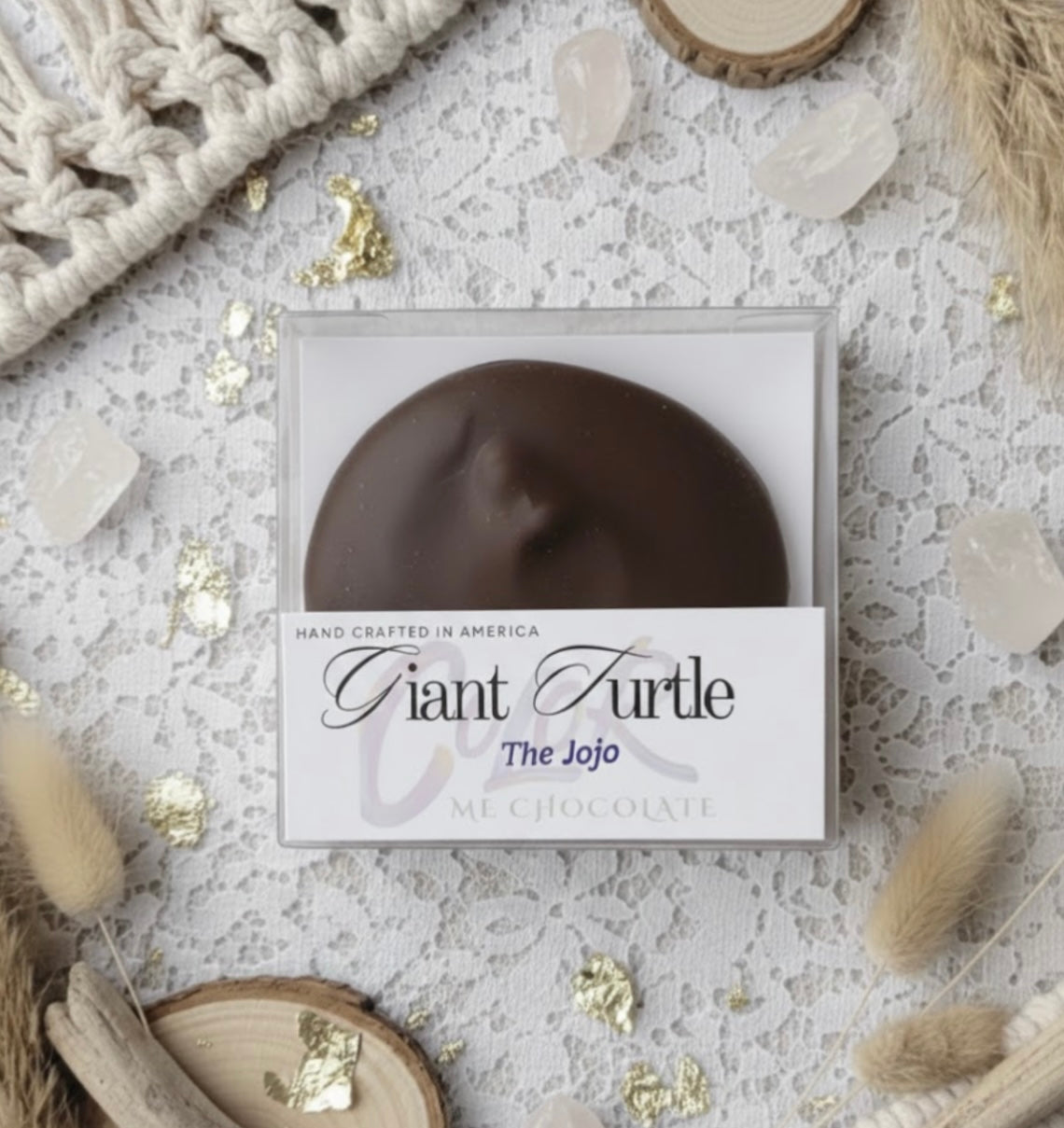 Chocolate turtle in a box labeled 'Giant Turtle' on a decorative surface with crystals and macrame.