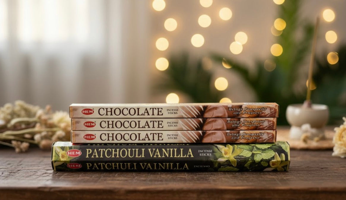 Stack of HEM incense sticks with 'Chocolate' and 'Patchouli Vanilla' labels on a wooden surface with a blurred background.
