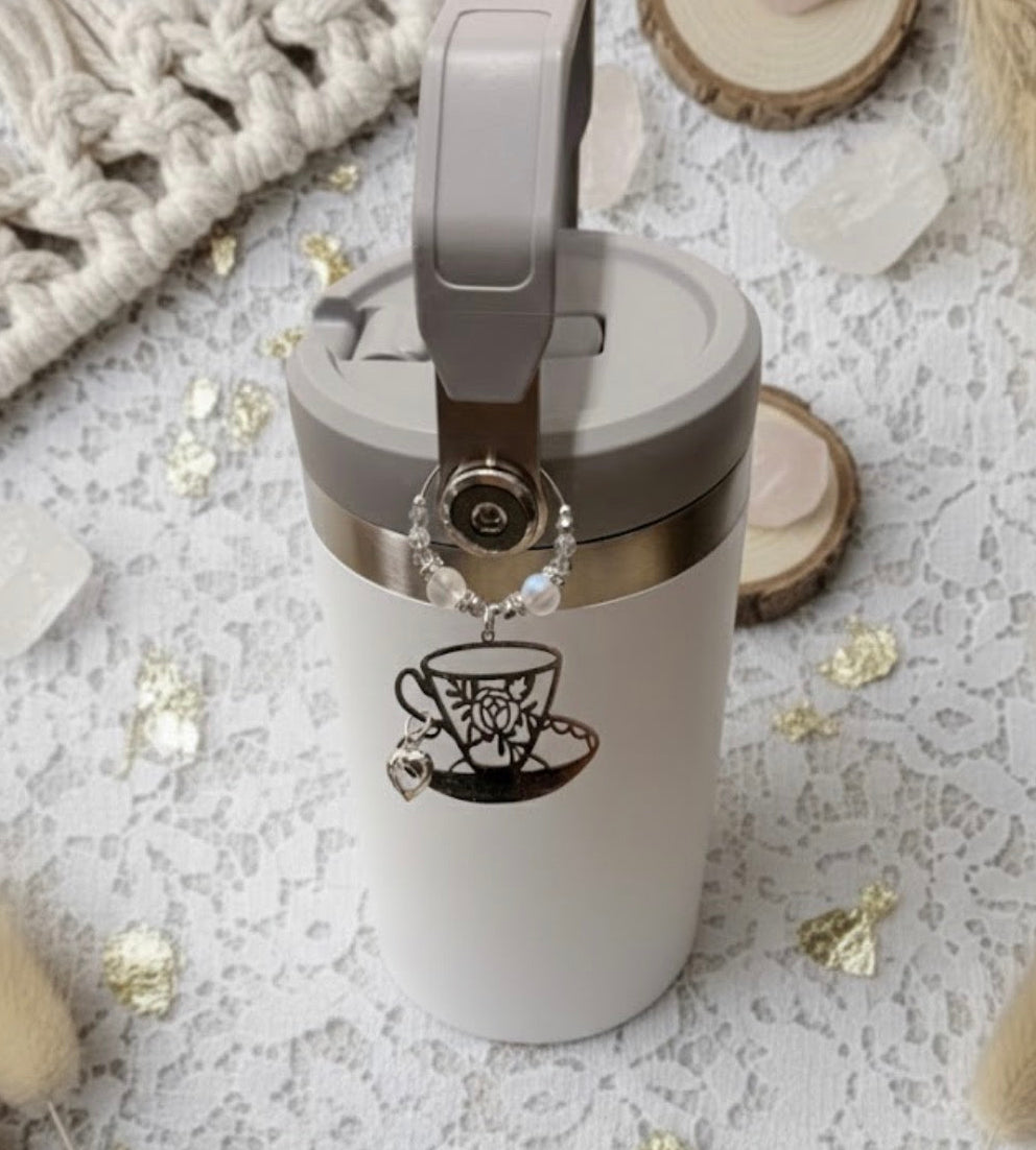 White tumbler with gray lid and decorative teacup charm on a textured surface