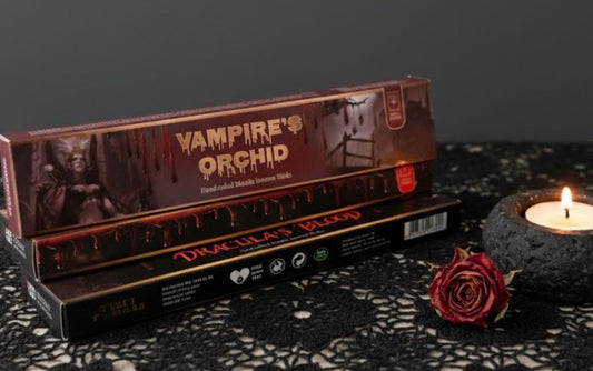 Vampire's Orchid and Dracula’s Blood incense with a candle and rose on a dark surface