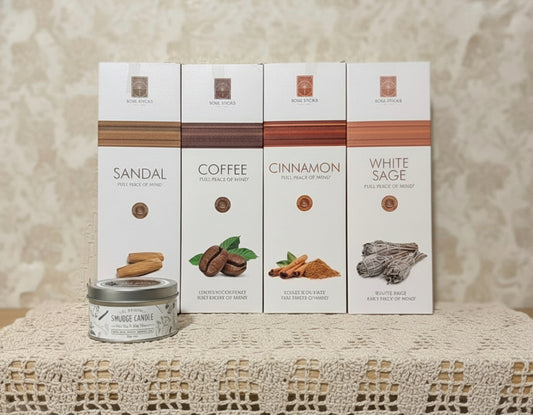 Candle and 4 boxes of incense labeled Sandal, Coffee, Cinnamon, and White Sage on a textured surface