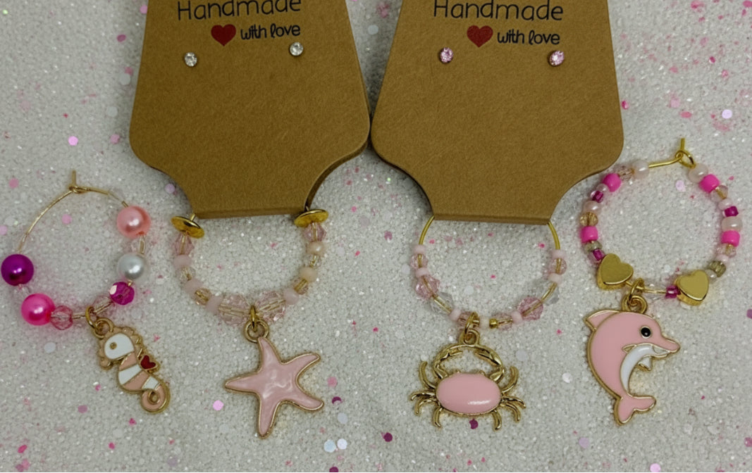 wine glass charms with oceanic charms on a textured surface. wine glass charms ocean life with earrings. dolphin. starfish. seahorse. crab. pretty in pink. 
