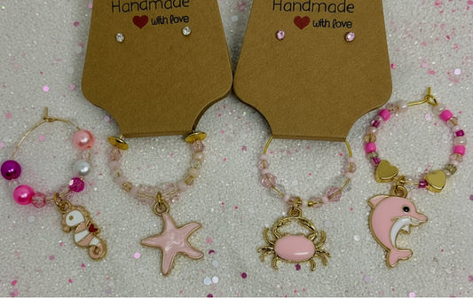 wine glass charms with oceanic charms on a textured surface. wine glass charms ocean life with earrings. dolphin. starfish. seahorse. crab. pretty in pink. 