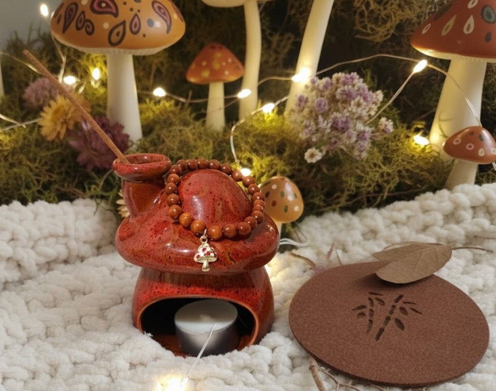 Decorative scene with a red ceramic incense burner, mushrooms, and flowers on a white stone surface. Wooden mushroom charm bracelet. 