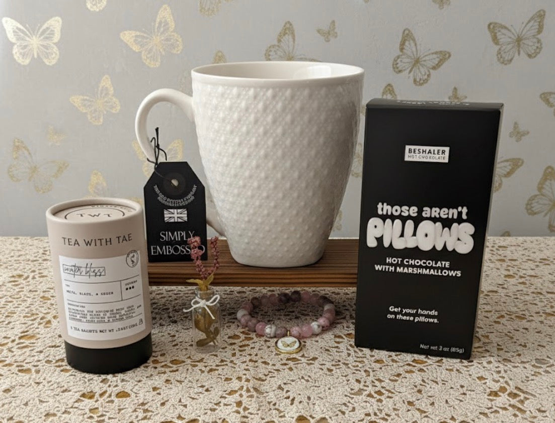 White textured mug, tea canister, and box of hot chocolate on a surface with decorative butterfly wallpaper.